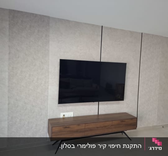 קיר עם טלוויזיה תלויה וארון עץ מתחת